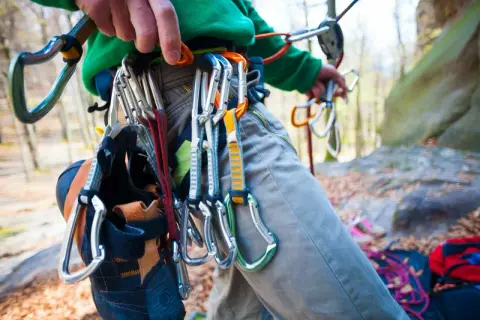 Kletterer mit Ausrüstung für trad klettern, Kletterschuhe hängen am Gurt.