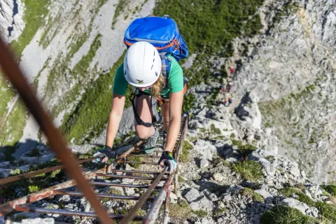 Bergsteigerin klettert eine Leiter hinauf. Die Klettersteige haben unterschiedliche Schwierigkeitsgrade, diese hier scheint mittelschwer zu sein.