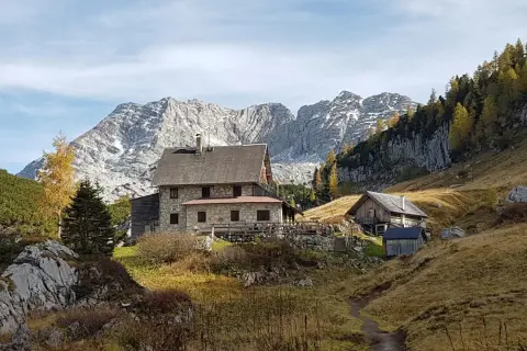 Steinhäuser und Holzhütten am Fuße eines majestätischen, schneebedeckten totes Gebirge. Herbstliche Bäume leuchten golden.