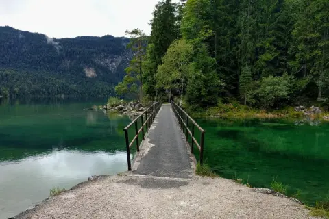 Ein schmaler Steg führt über das smaragdgrüne Wasser des Eibsees. Der eibsee rundweg lädt zu einer Erkundung der malerischen Natur ein, umgeben von dichten Wäldern und Bergen.