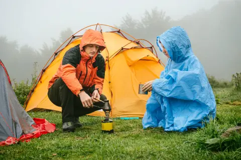 Zwei Camper im Regen bereiten sich eine warme Mahlzeit zu, während das Zelt trocknen muss.