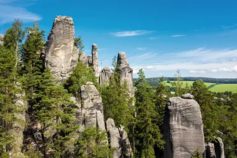 Felsformationen in Tschechien, ideal zum Klettern, umgeben von grünen Bäumen und einem blauen Himmel.