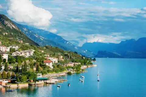 Ein malerisches Dorf am Gardasee in Norditalien, mit Häusern, die sich an den grünen Hang schmiegen, und dem tiefblauen Wasser, das zum Segeln einlädt.