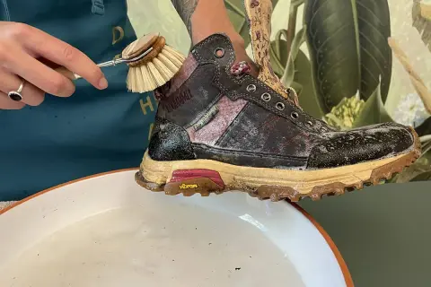 Schmutzige Wanderschuhe reinigen mit einer Bürste und Seifenwasser.
