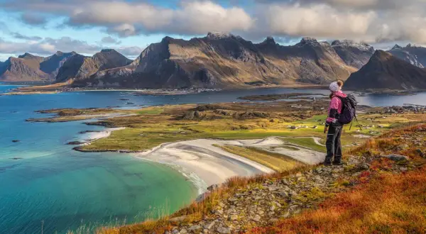 Wanderer blickt auf malerische Küste mit Bergen. Die Lofoten zeigen sich von ihrer besten Reisezeit-Seite.