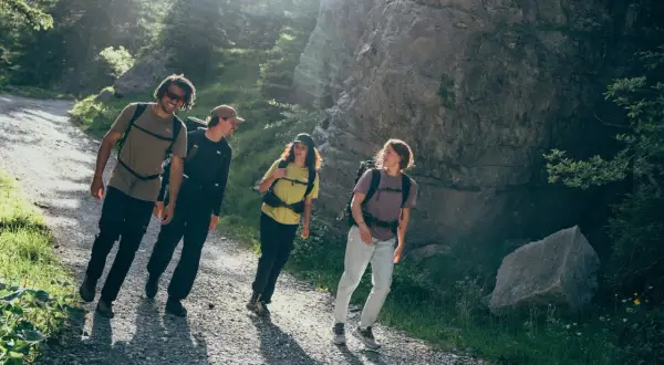 Vier Freunde genießen das Wandern auf einem sonnigen Bergpfad. Das ist die wahre Definition von Wandern: Natur, Gemeinschaft und Bewegung.