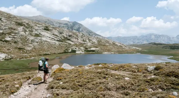 Wanderer auf dem GR20, Korsika, auf dem Weg zu einer Hütte. Bergsee und felsige Landschaft.