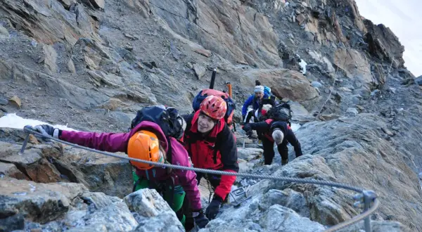 Bergsteiger seilen sich auf dem Weg zur Wildspitze ab. Ein Mann im roten Anzug lächelt in die Kamera.