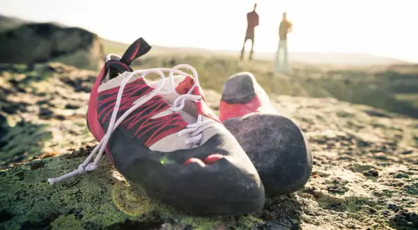 Boulderschuhe ruhen auf moosbewachsenem Fels. Im Hintergrund stehen zwei Kletterer. Zeit für eine Wäsche nach dem Abenteuer.
