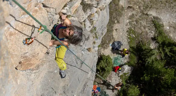 Frau klettert in Briançon, konzentriert sich auf den nächsten Griff. Unten warten Kletterer und Ausrüstung.