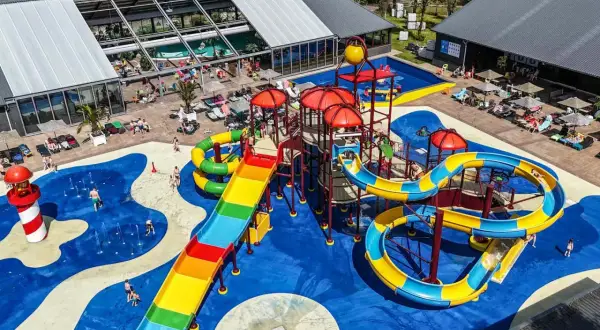 Bunter Wasserrutschen-Spaß auf einem Campingplatz mit Pool im Allgäu. Kinder planschen und rutschen ausgelassen.
