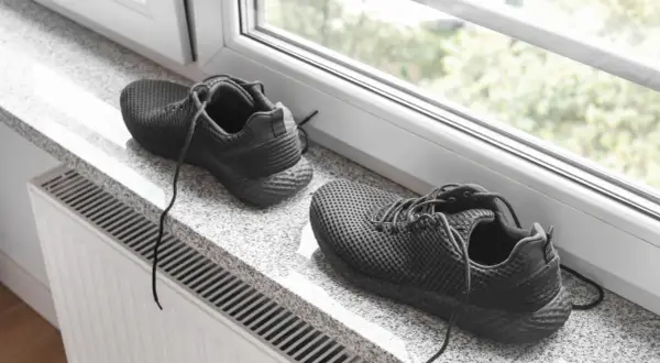 Schwarze Turnschuhe trocknen auf einem Fensterbrett über einer Heizung.