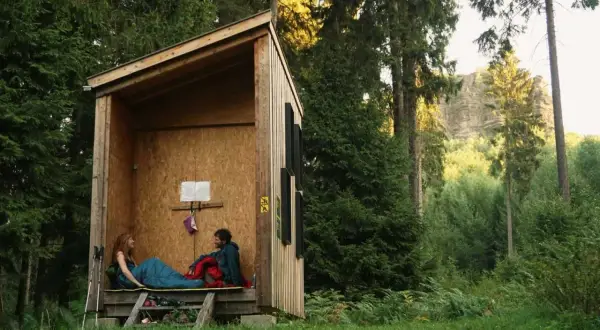 Ein Paar entspannt in einer Schutzhütte im Wald. Hier darf man im Wald schlafen und die Natur genießen.