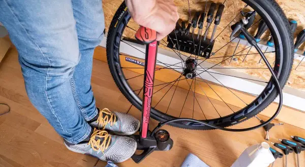 Fahrradreifen aufpumpen mit einer roten Luftpumpe. Werkzeug und eine Flasche Flüssigkeit liegen bereit.