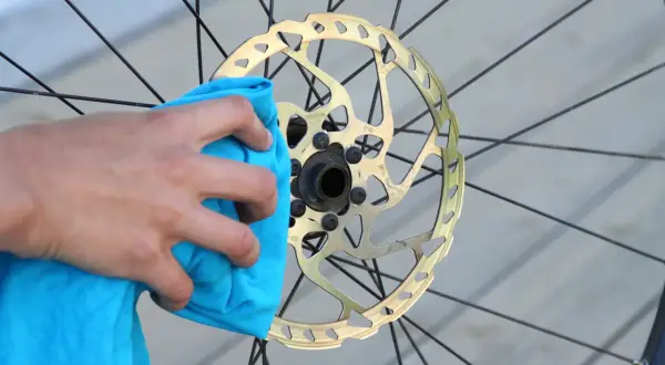 Hand reinigt goldene Fahrrad-Scheibenbremse mit blauem Tuch. Perfekt für den Wechsel der Scheibenbremse am Fahrrad.