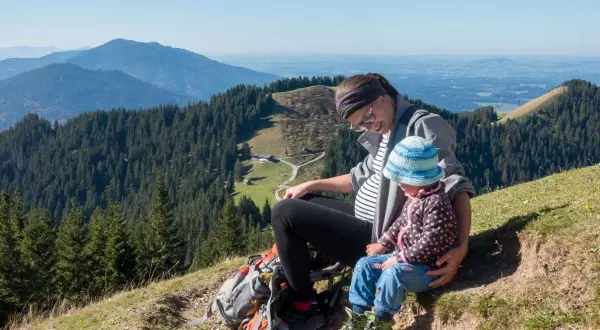 Schwangerschaft und Wandern: Eine Frau mit Babybauch und Kind genießen die Aussicht auf Berge und Wälder.
