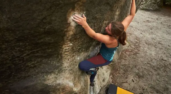 Eine Frau klettert an einem Felsen in Fontainebleau. Sie nutzt ihre Kraft und Technik beim Bouldern.