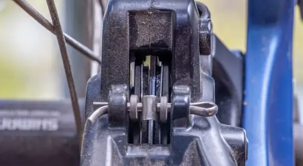 Nahaufnahme einer Fahrradbremse. Die Bremsbeläge schleifen einseitig am Rotor. Staub und Schmutz sind sichtbar.