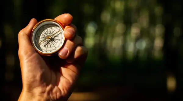 Eine Hand hält einen goldenen Kompass, der die Himmelsrichtungen anzeigt. So lernt man, wie liest man einen Kompass.