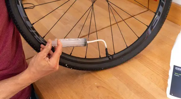 Mit einer Spritze wird Dichtmilch in den Fahrradreifen gefüllt, um die Laufrichtung zu optimieren und Pannen zu vermeiden.