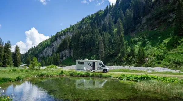 Wohnmobil am Bergsee. Hier darf man in der Schweiz wild campen, umgeben von grünen Hängen und Nadelbäumen.