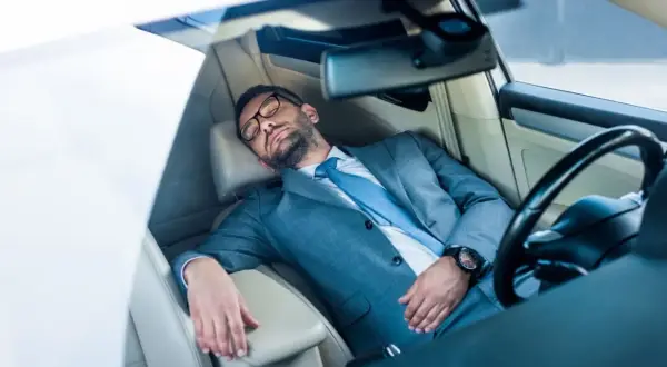 Ein Geschäftsmann im Anzug schläft im Auto. Ob man in Italien im Auto schlafen darf, ist eine andere Frage.
