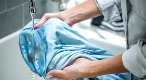 Hände spülen Matsch aus Kleidung unter fließendem Wasser.
