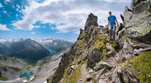 Wanderer auf einem steinigen Pfad der Peter Habeler Runde mit Blick auf türkisfarbene Bergseen und schneebedeckte Gipfel.