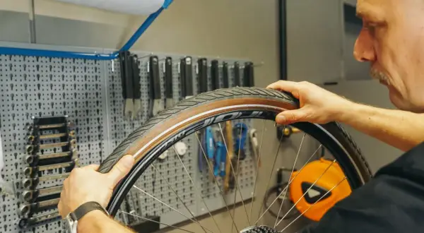 Mann wechselt den Fahrradschlauch. Werkzeugwand im Hintergrund.
