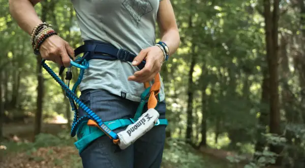 Person legt Klettersteigset an. Sicherungsgurt mit Karabiner und Seil im Wald.