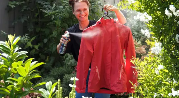 Frau sprüht rote Softshelljacke im Garten ein, um sie zu waschen und zu imprägnieren.