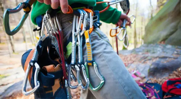 Kletterer mit Ausrüstung für trad klettern, Kletterschuhe hängen am Gurt.