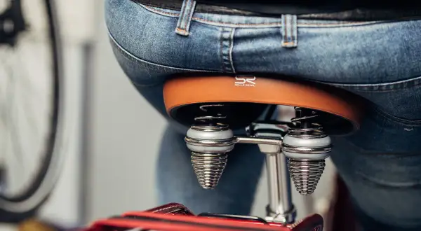 Person sitzt auf einem Fahrradsattel. Der Sattel ist braun und hat Federn. Der Sattel zu breit für Komfort.