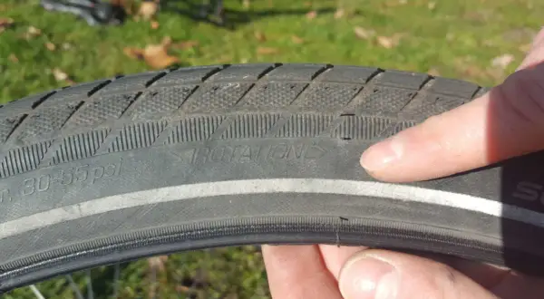 Finger zeigt auf abgefahrenen Fahrradreifen mit der Aufschrift "ROTATION". Zeit, wann Fahrradreifen wechseln.
