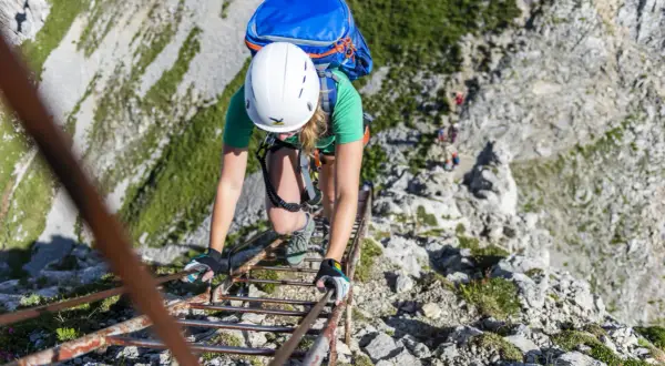 Bergsteigerin klettert eine Leiter hinauf. Die Klettersteige haben unterschiedliche Schwierigkeitsgrade, diese hier scheint mittelschwer zu sein.