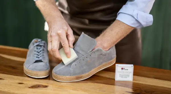 Mann reinigt graue Nubukleder-Sneaker mit einem speziellen Radierer.