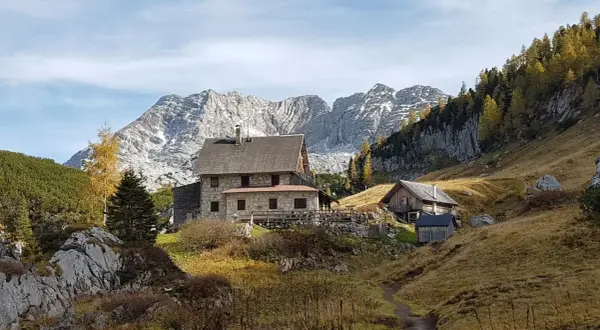 Steinhäuser und Holzhütten am Fuße eines majestätischen, schneebedeckten totes Gebirge. Herbstliche Bäume leuchten golden.