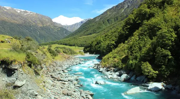 Türkisfarbener Fluss schlängelt sich durch ein Tal mit bewaldeten Hängen und schneebedeckten Gipfeln, die an Roy's Peak erinnern.