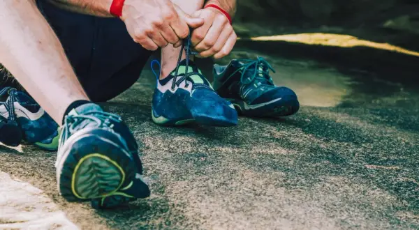 Hände schnüren blaue Kletterschuhe, bereit für den nächsten Aufstieg. Die Füße sind für das Klettern vorbereitet, um die Felsen zu meistern.