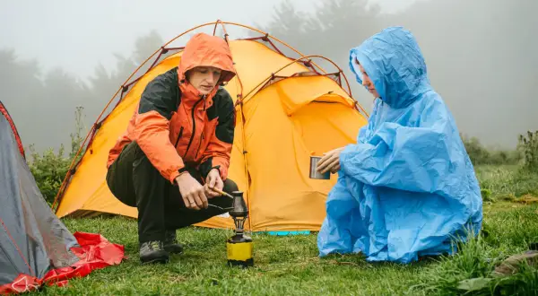Zwei Camper im Regen bereiten sich eine warme Mahlzeit zu, während das Zelt trocknen muss.