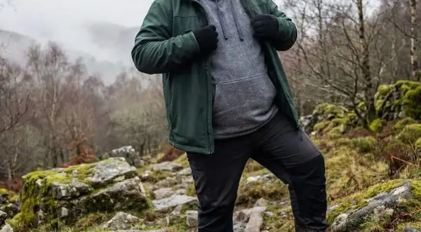 Mann in grüner Jacke und grauer Kapuzenjacke wandert durch felsiges Gelände. Die Jacke ist softshell wasserdicht und schützt vor dem Wetter.