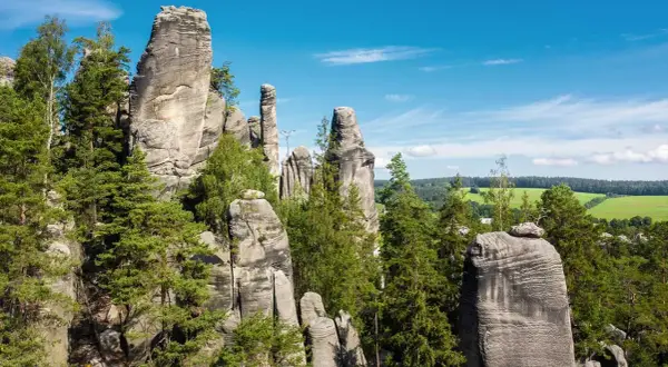 Felsformationen in Tschechien, ideal zum Klettern, umgeben von grünen Bäumen und einem blauen Himmel.