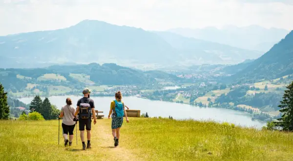 Drei Personen genießen eine leichte Wanderung mit Blick auf einen See und Berge.
