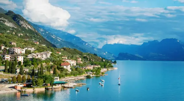 Ein malerisches Dorf am Gardasee in Norditalien, mit Häusern, die sich an den grünen Hang schmiegen, und dem tiefblauen Wasser, das zum Segeln einlädt.