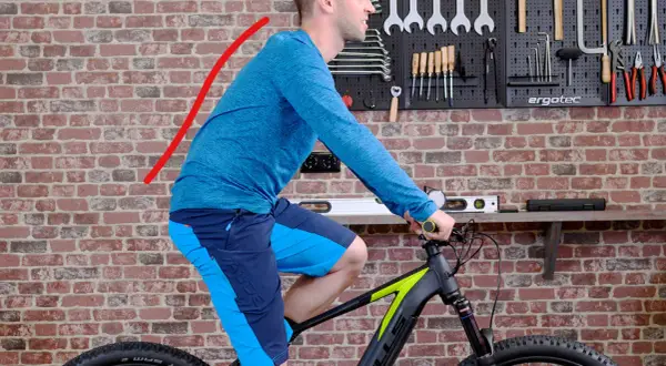 Mann auf einem Fahrrad in aufrechter Sitzposition, der Rücken ist leicht gekrümmt. Werkzeugwand im Hintergrund.