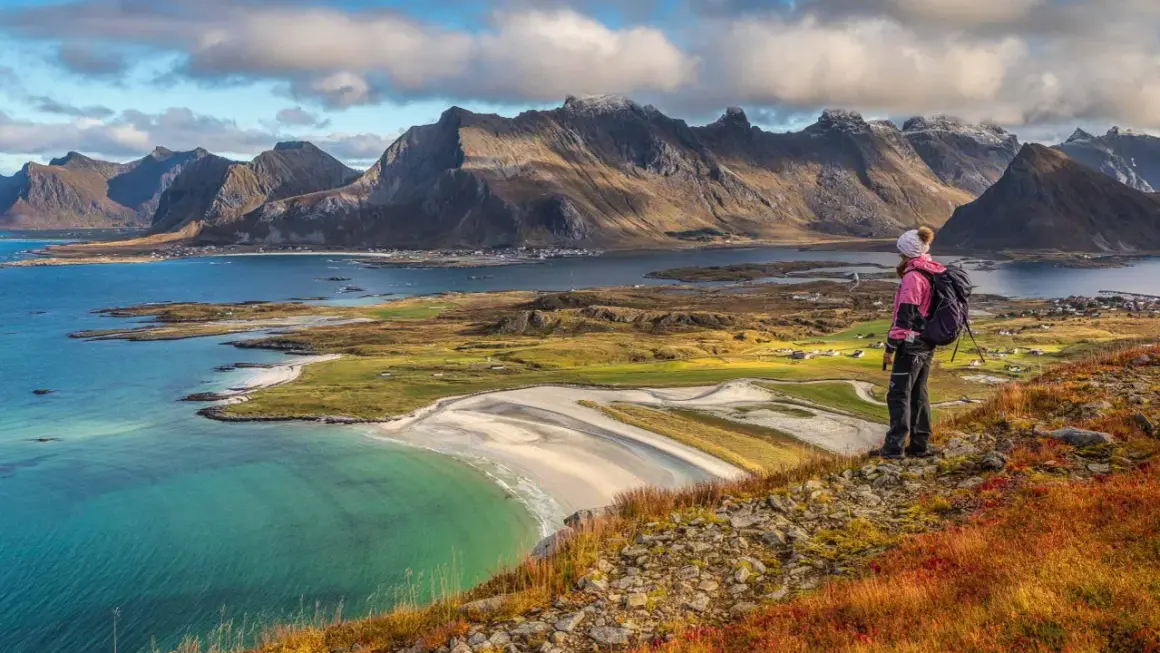 Wanderer blickt auf malerische Küste mit Bergen. Die Lofoten zeigen sich von ihrer besten Reisezeit-Seite.