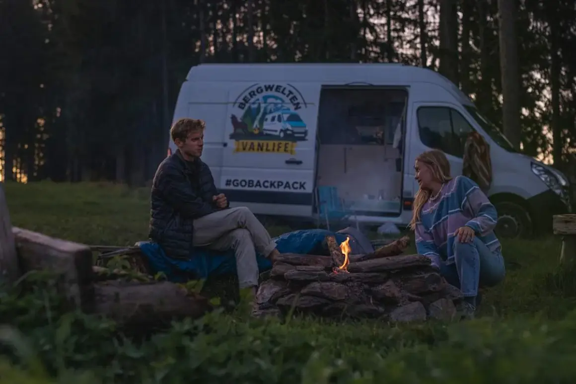 Ein Paar genießt das Lagerfeuer beim wildcampen Bayern. Ihr Van steht im Hintergrund, bereit für das nächste Abenteuer.