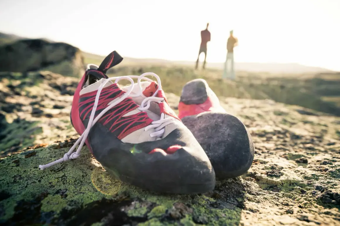Boulderschuhe ruhen auf moosbewachsenem Fels. Im Hintergrund stehen zwei Kletterer. Zeit für eine Wäsche nach dem Abenteuer.