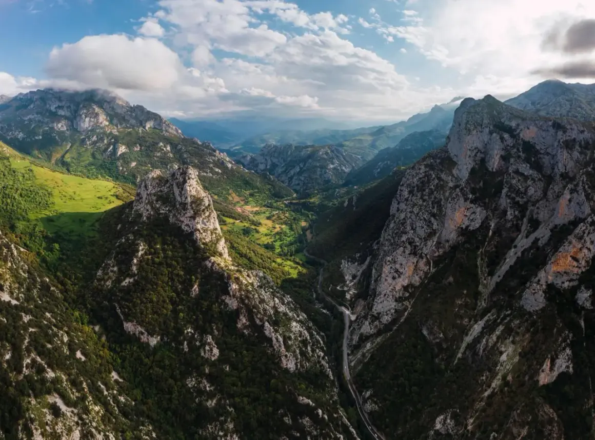 Majestätische Berge der Picos de Europa, grüne Täler und eine Straße, die sich durch die Schlucht schlängelt.