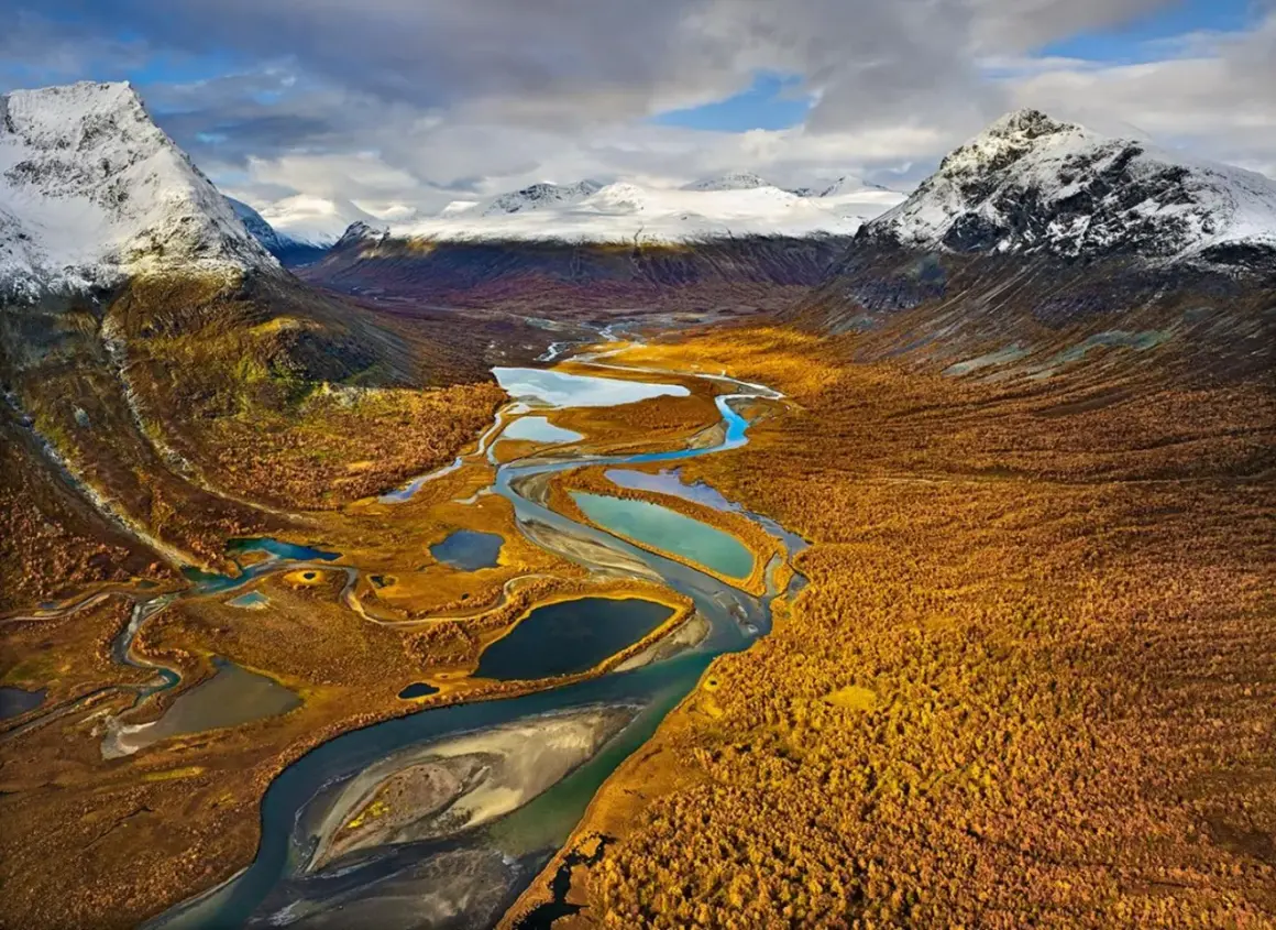Herbstliche Landschaft mit Flüssen und Seen, ideal für fernwanderwege schweden. Schneebedeckte Berge im Hintergrund.